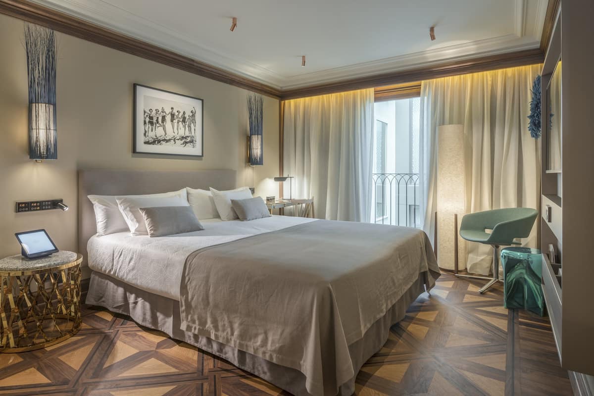 A hotel room with a large bed, a desk with a laptop, a chair, and a view of the outdoors through the window.