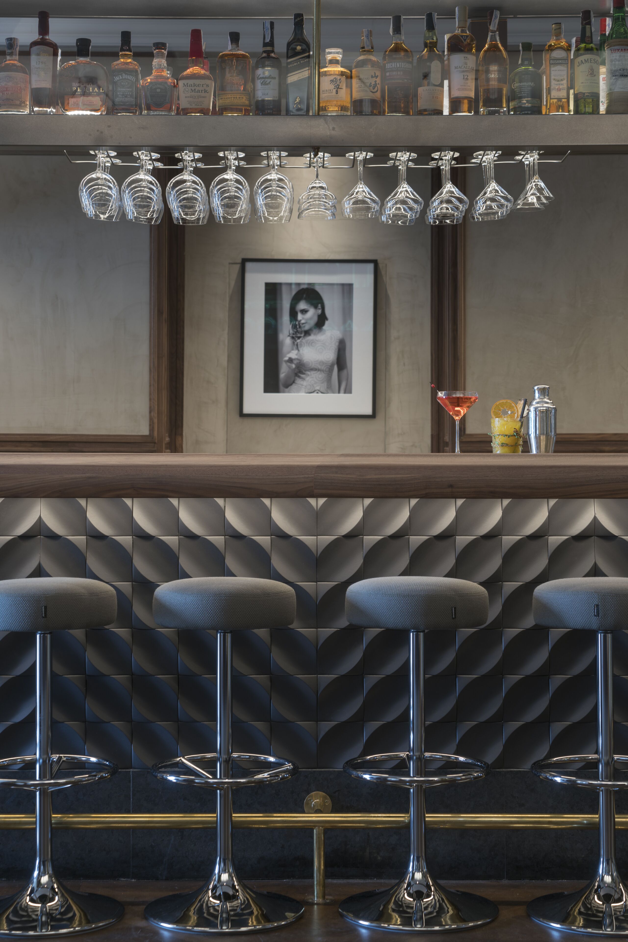 Zona de bar con diversas botellas de licor, una fotografía enmarco y taburetes de bar.
