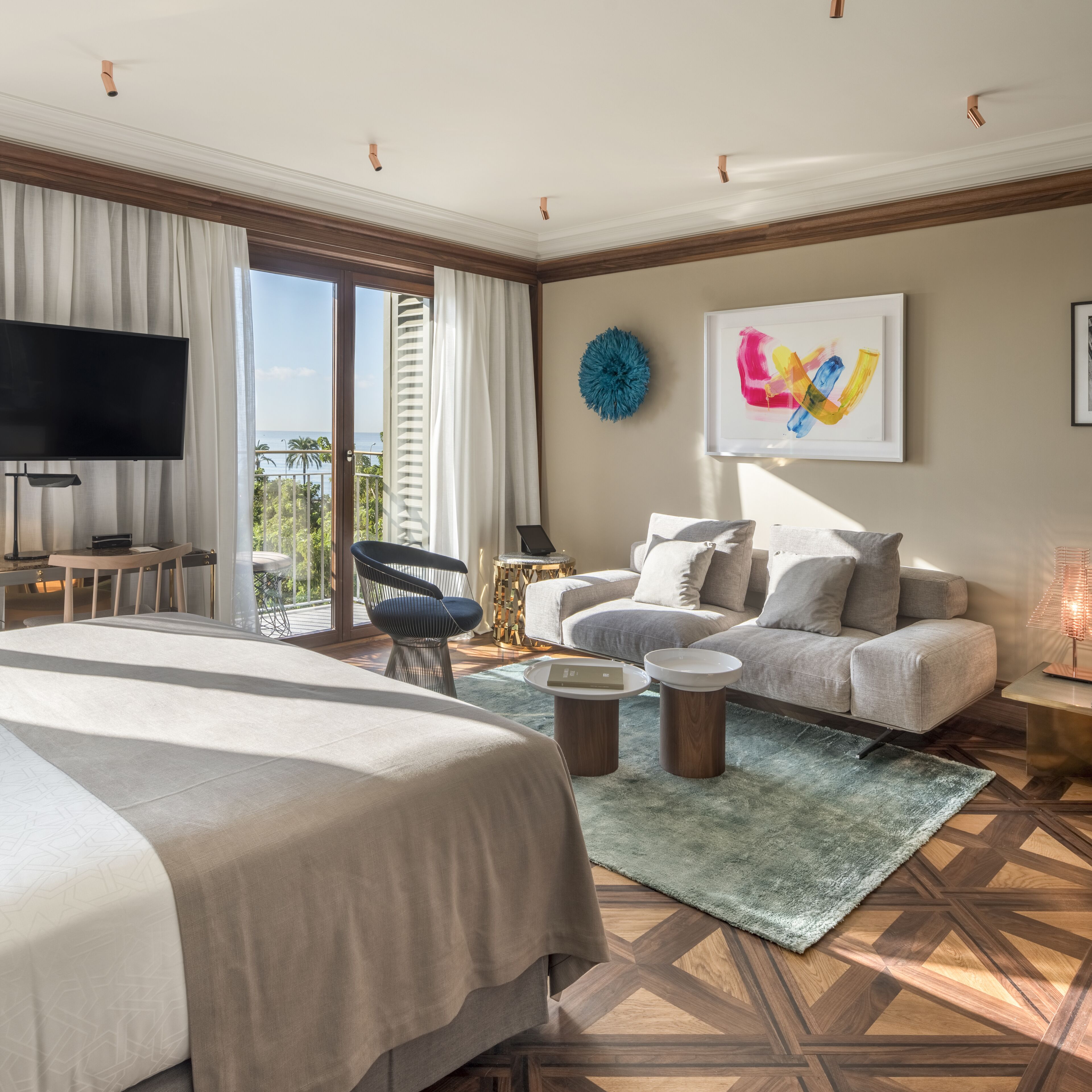 A modern hotel room with a large bed, a sofa, a TV, and a view of the ocean.
