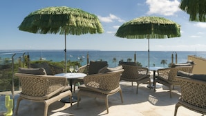 A terrace with wicker furniture, two thatched umbrellas, and a view of the sea. - Hotel El Llorenç Parc de la Mar - Adults Only (Palma de Mallorca)