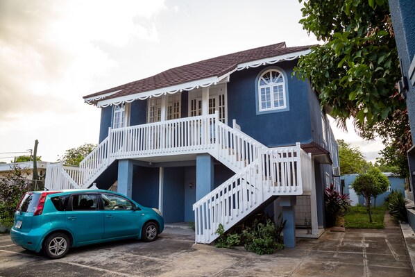 A two-story house with a white staircase and a blue car parked in the driveway.