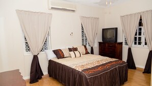 Une chambre à coucher avec un lit, des rideaux, une télévision et une commode en bois.