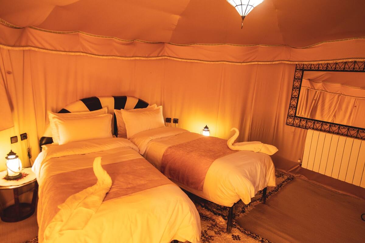 A hotel room with two beds, a nightstand with a lamp, and a decorative swan on the bed.