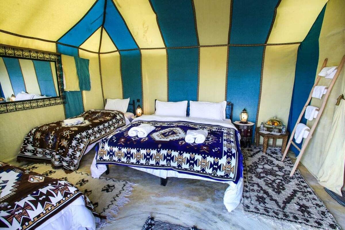 A tent-style room with two beds, each with patterned bedding, a mirror, and a small table with a lamp.