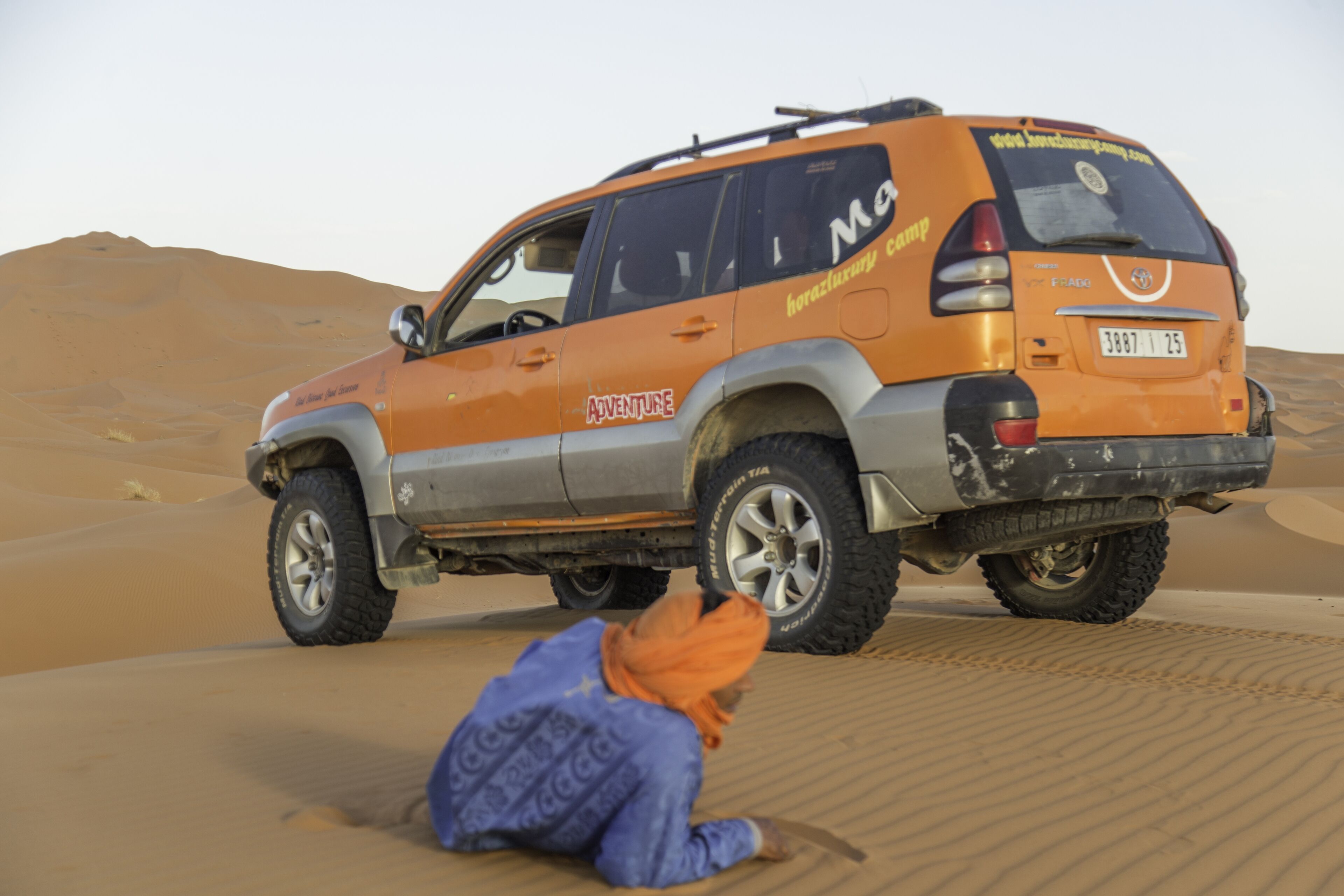 A desert SUV with "Adventure" and "MGM" branding parked on sand dunes.