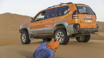 A desert SUV with "Adventure" and "MGM" branding parked on sand dunes.