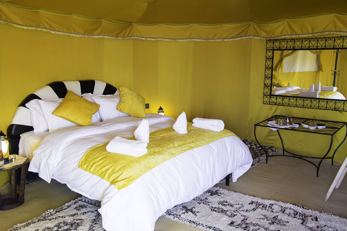 A hotel room with a bed, a nightstand, a table, and a mirror.