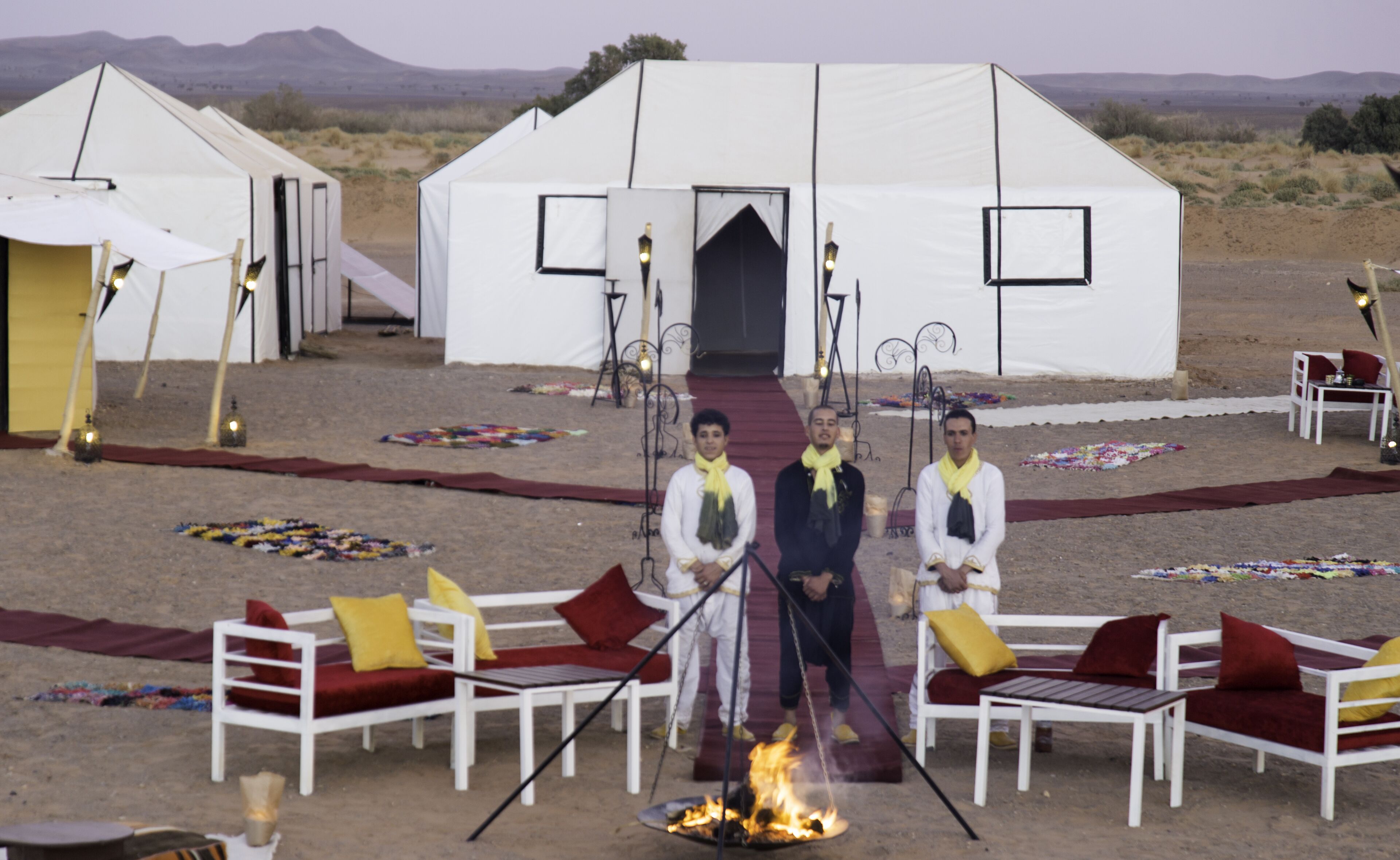 A desert camp with tents, a fire pit, and seating areas.