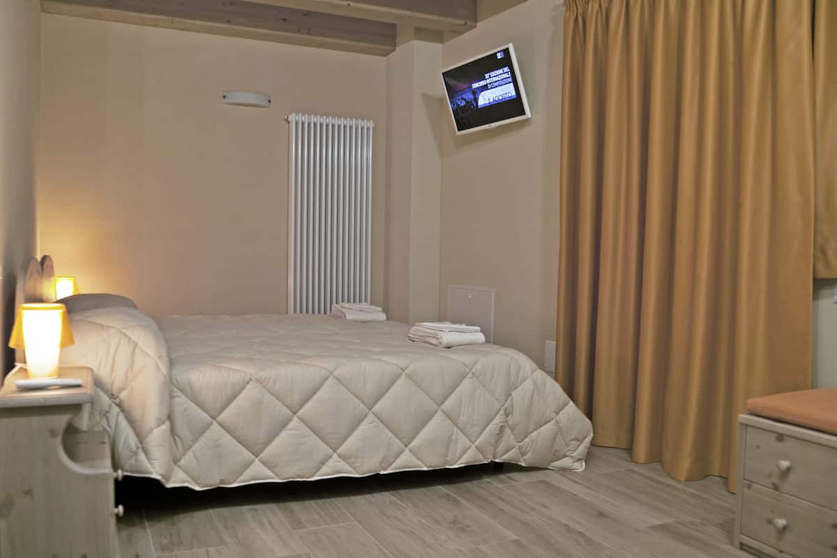 Une chambre d’hôtel avec un lit, un téléviseur fixé au mur, une fenêtre avec des stores et un rideau.