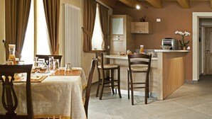 Un espace de vie chaleureux comprenant une table à manger, deux chaises, un canapé, un coin cuisine avec un plan de travail et une porte en bois.