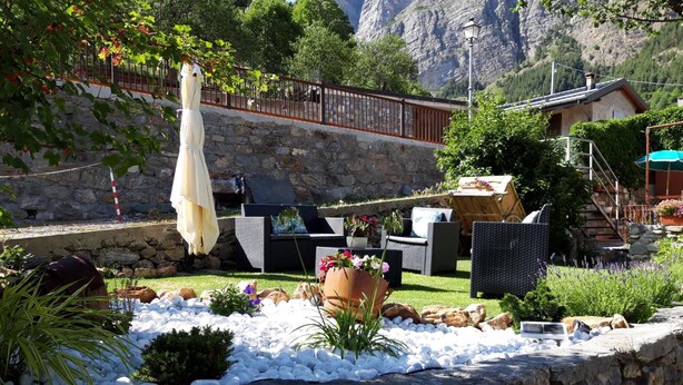 Un mur de pierre bordé d’un jardin agrémenté de galets blancs, d’une chaise en osier, d’une table avec des plantes en pot et offrant une vue sur une montagne en arrière-plan.