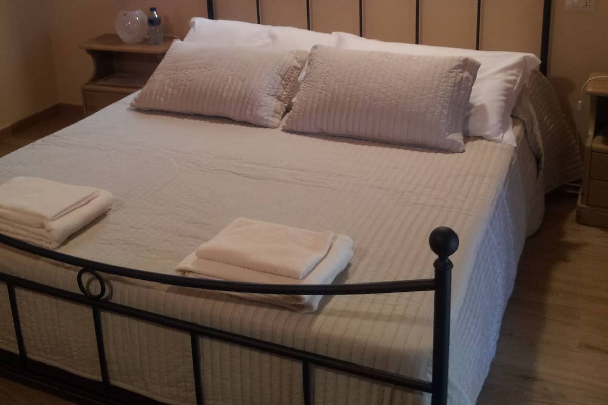Un lit bien fait, avec un cadre en métal, une table de chevet avec une lampe et une fenêtre avec des rideaux.