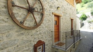 Un bâtiment en pierre avec une grande roue en bois fixée au mur, une porte en bois et un petit balcon doté d’une rambarde en métal.