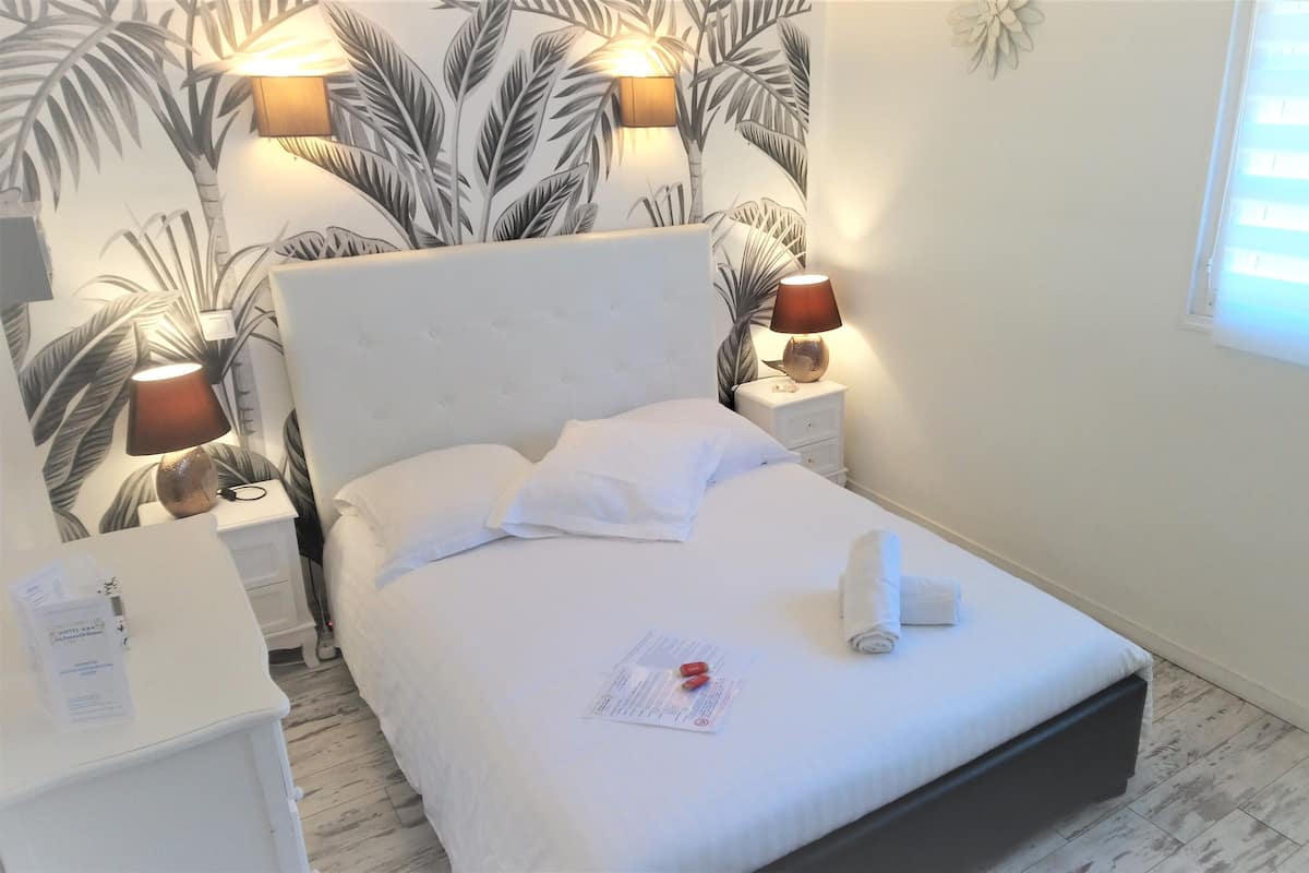 Una cama bien hecha con sábanas blancas, una lámpara de noche y una mesita de noche con lámpara.