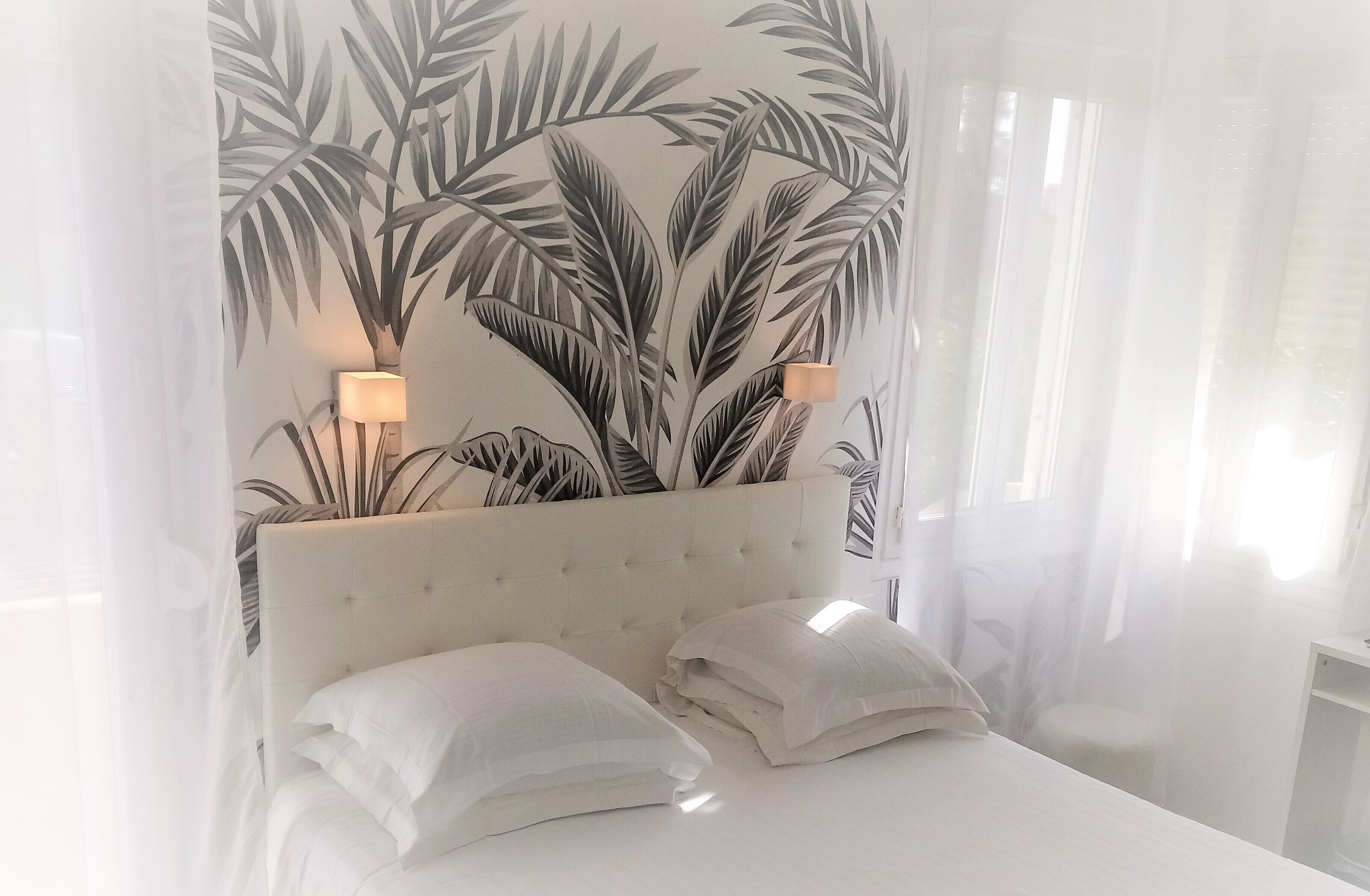 A bed with white bedding and two pillows, a tufted headboard, and a wall with a tropical leaf pattern.