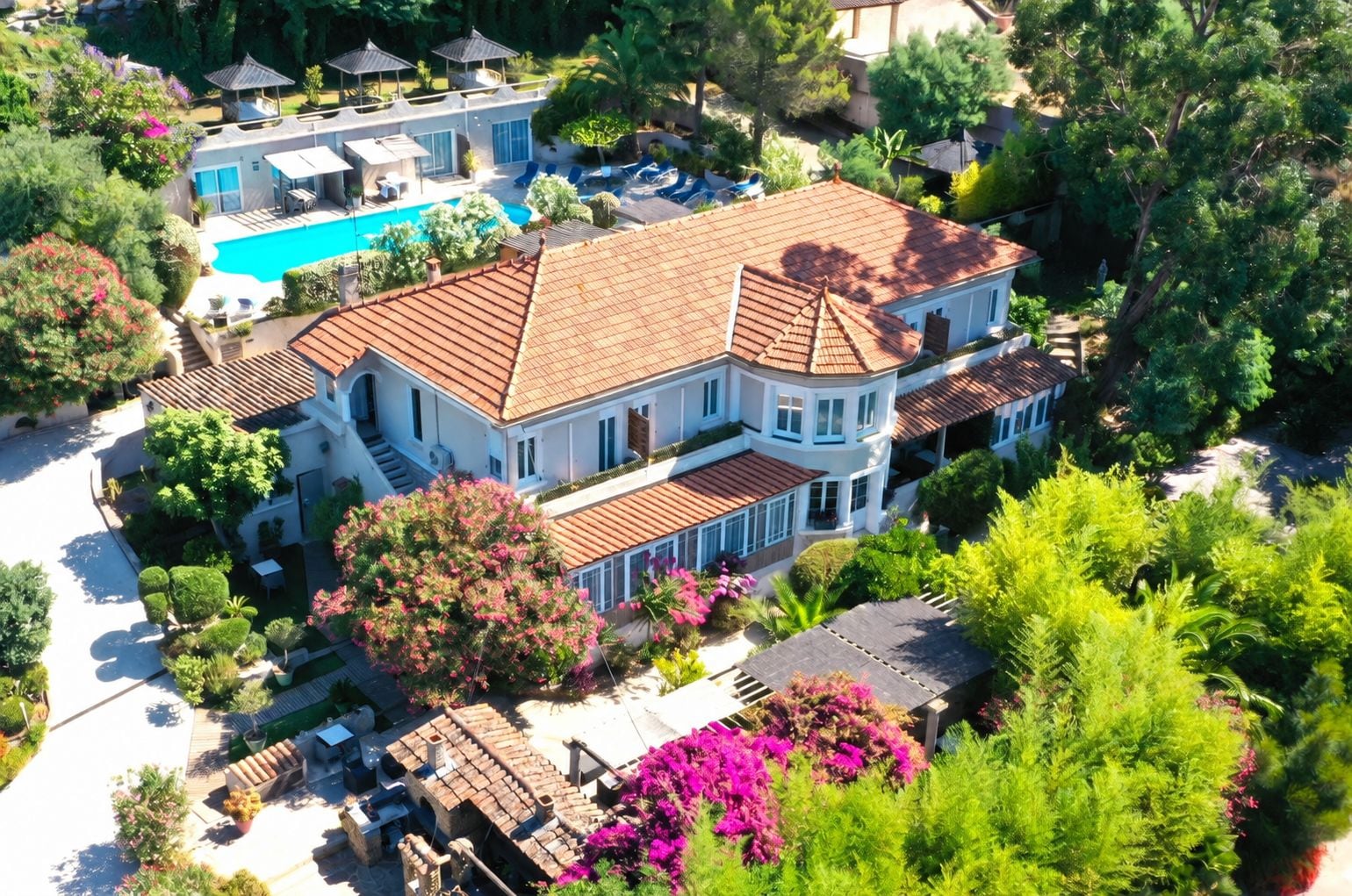 Une grande maison à deux étages avec une piscine, entourée d’une végétation luxuriante et d’un jardin bien entretenu.