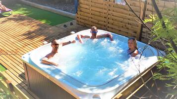 Un bain à remous où se trouvent trois personnes, entouré d’une terrasse en bois et d’une clôture en bois.