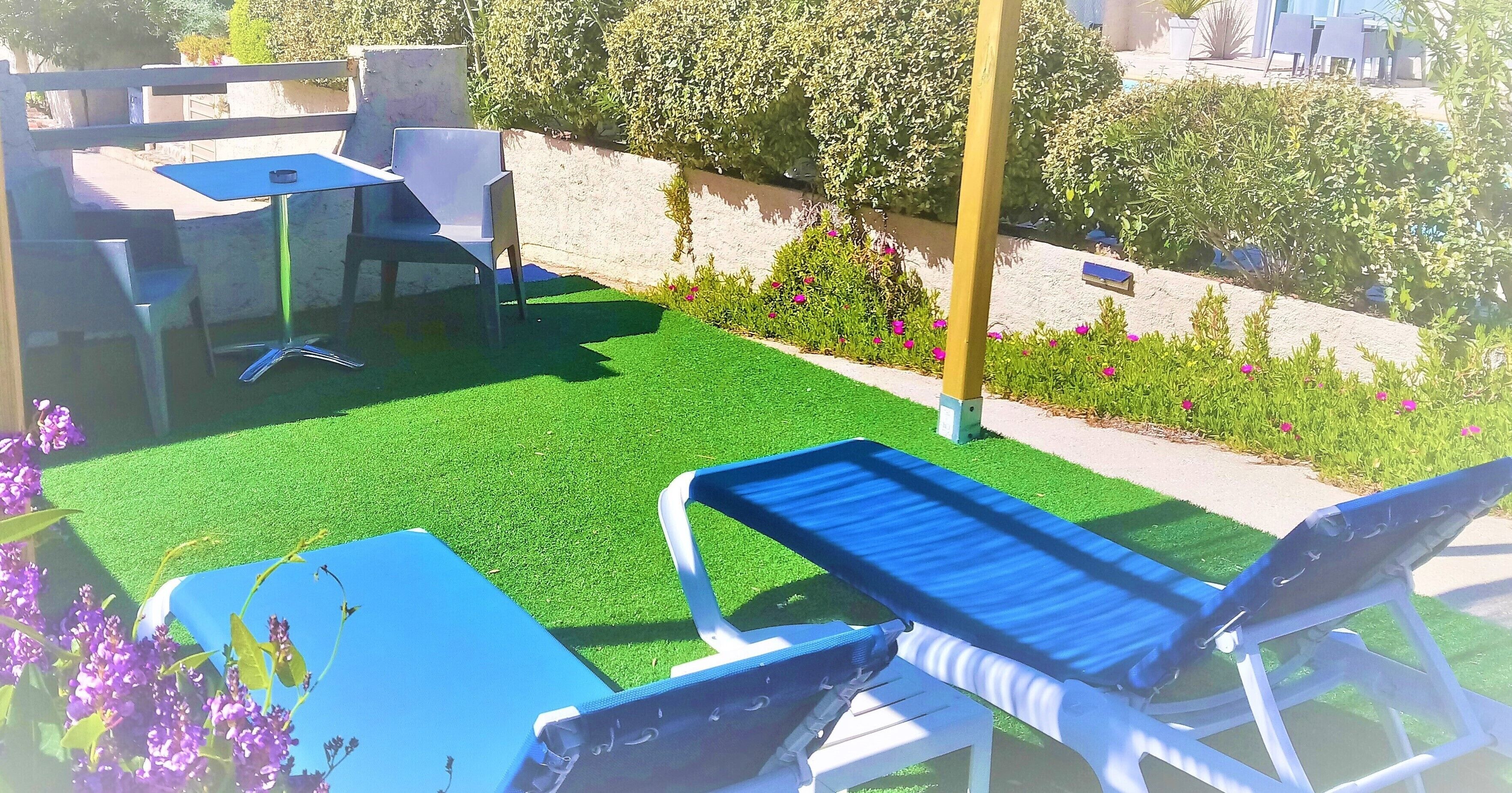 A patio with a table and chairs, artificial grass, and a flower bed.