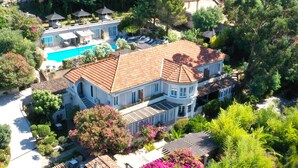 Una casa grande de dos pisos con piscina, rodeada de vegetación exuberante y un jardín cuidado.