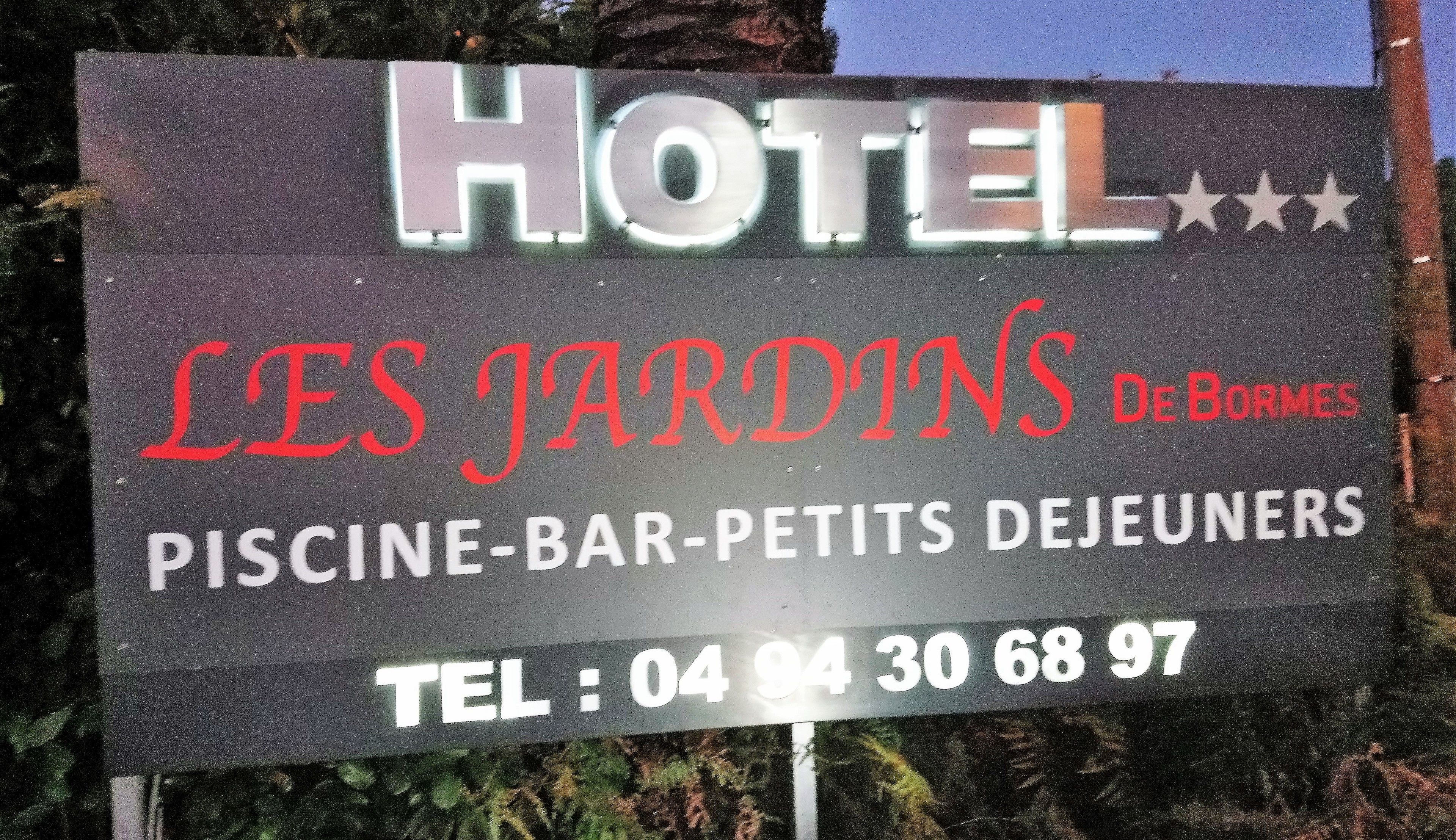 A hotel sign with the name "HOTEL LES JARDINS De Bormes" and amenities listed as "PISCINE-BAR-PETITS DEJEUNERS". The telephone number is also displayed.