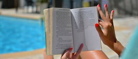 A person reading a book by a pool.