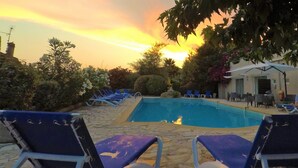 Un espace aménagé au bord de la piscine, avec des chaises longues et une petite piscine, le tout entouré de verdure et bordé d’un bâtiment doté d’une terrasse.