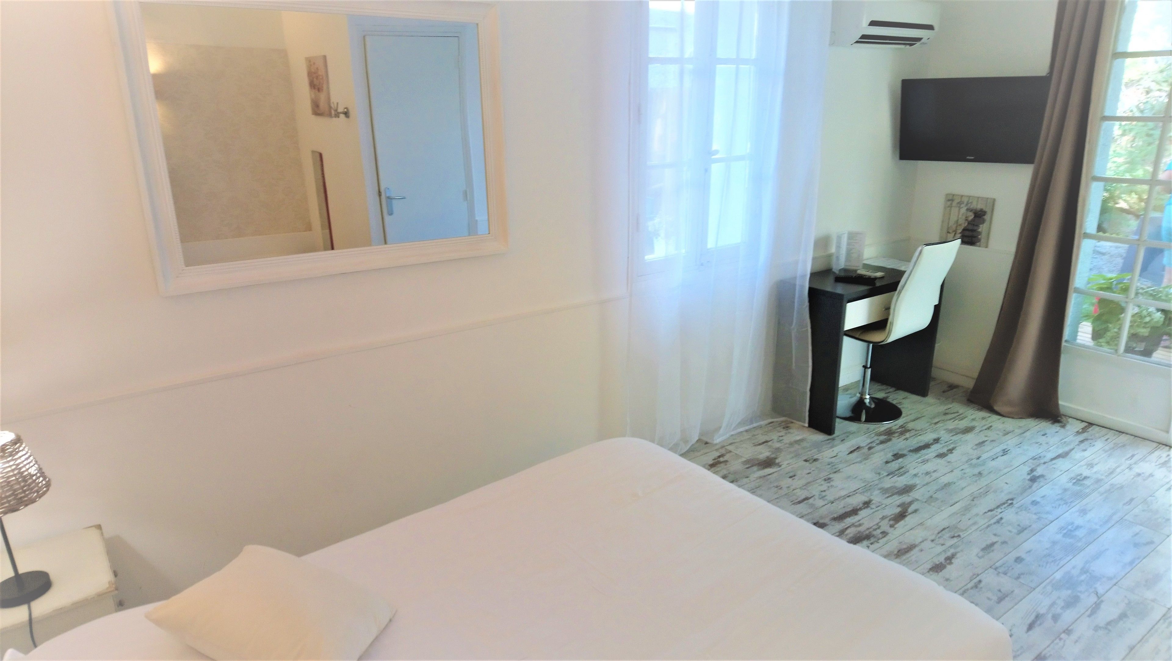 A hotel room with a bed, a desk with a chair, a TV, and a window with curtains.