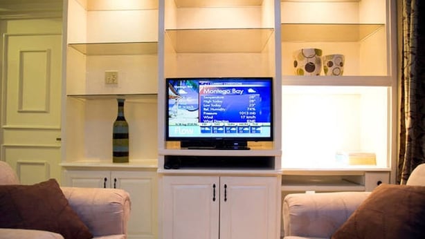 Un salón con un televisor mostrando información meteorológica para Montego Bay, un mueble blanco y dos sillones cómodos.