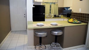 Una cocina compacta con una puerta blanca, un refrigerador negro, un microondas y dos taburetes de bar.