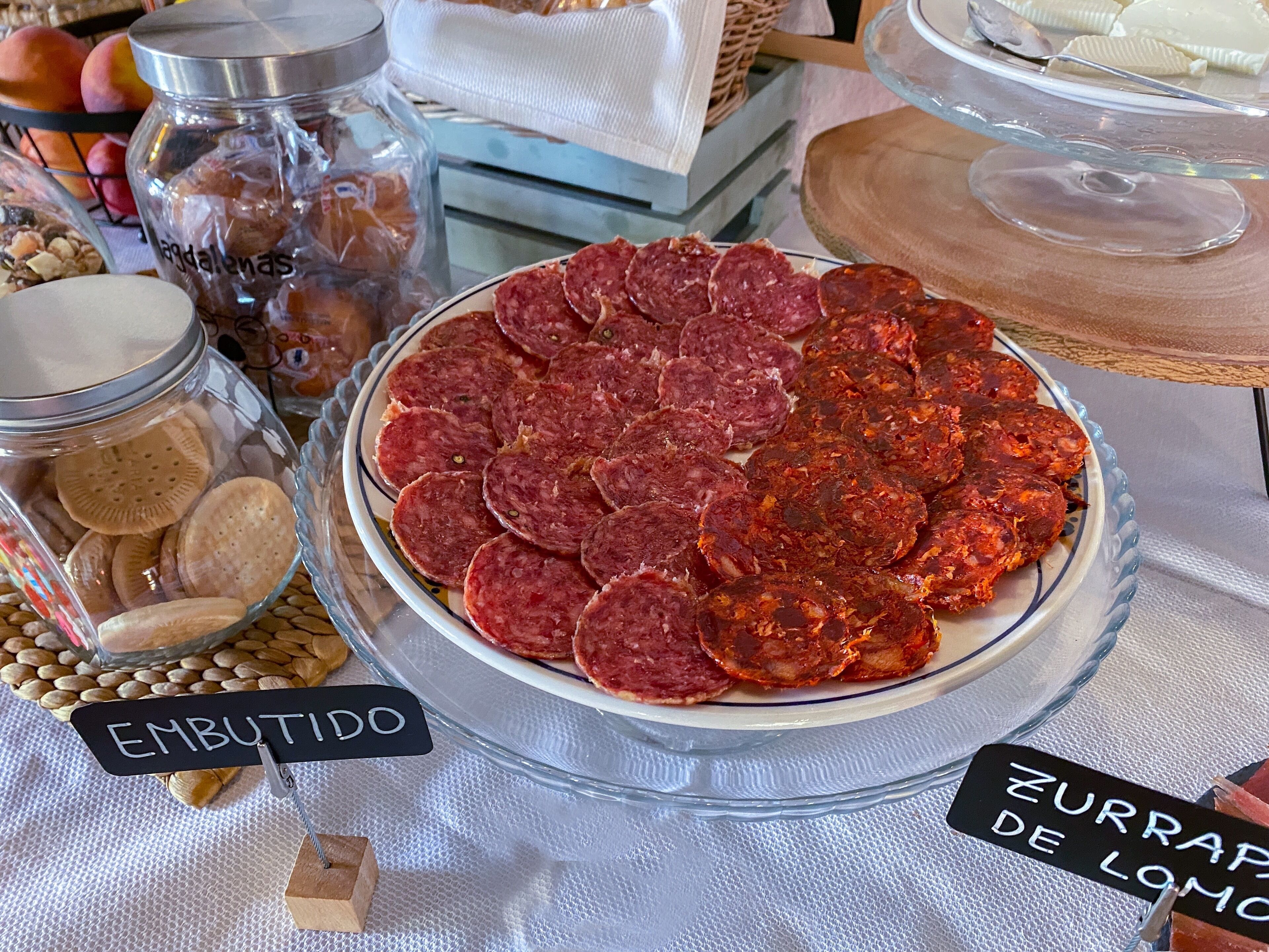 Una mesa con un plato de embutidos, un tarro de galletas y un recipiente con nueces.