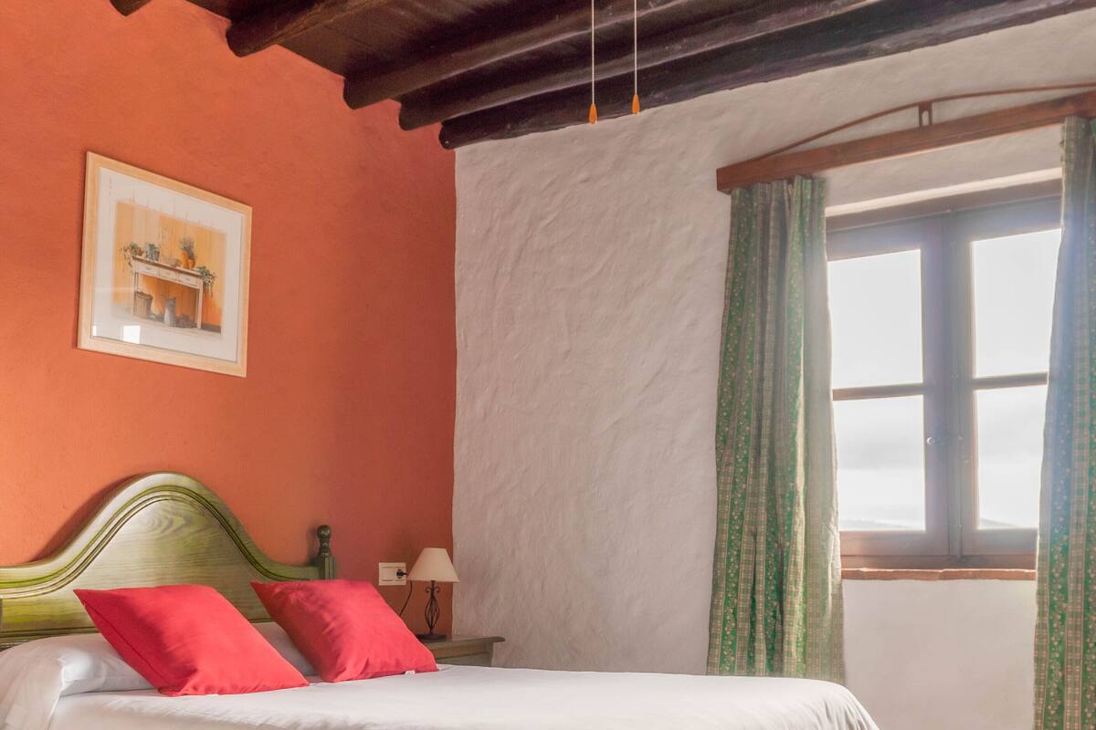 A bedroom with a bed, a ceiling fan, a window with curtains, and a framed picture on the wall.