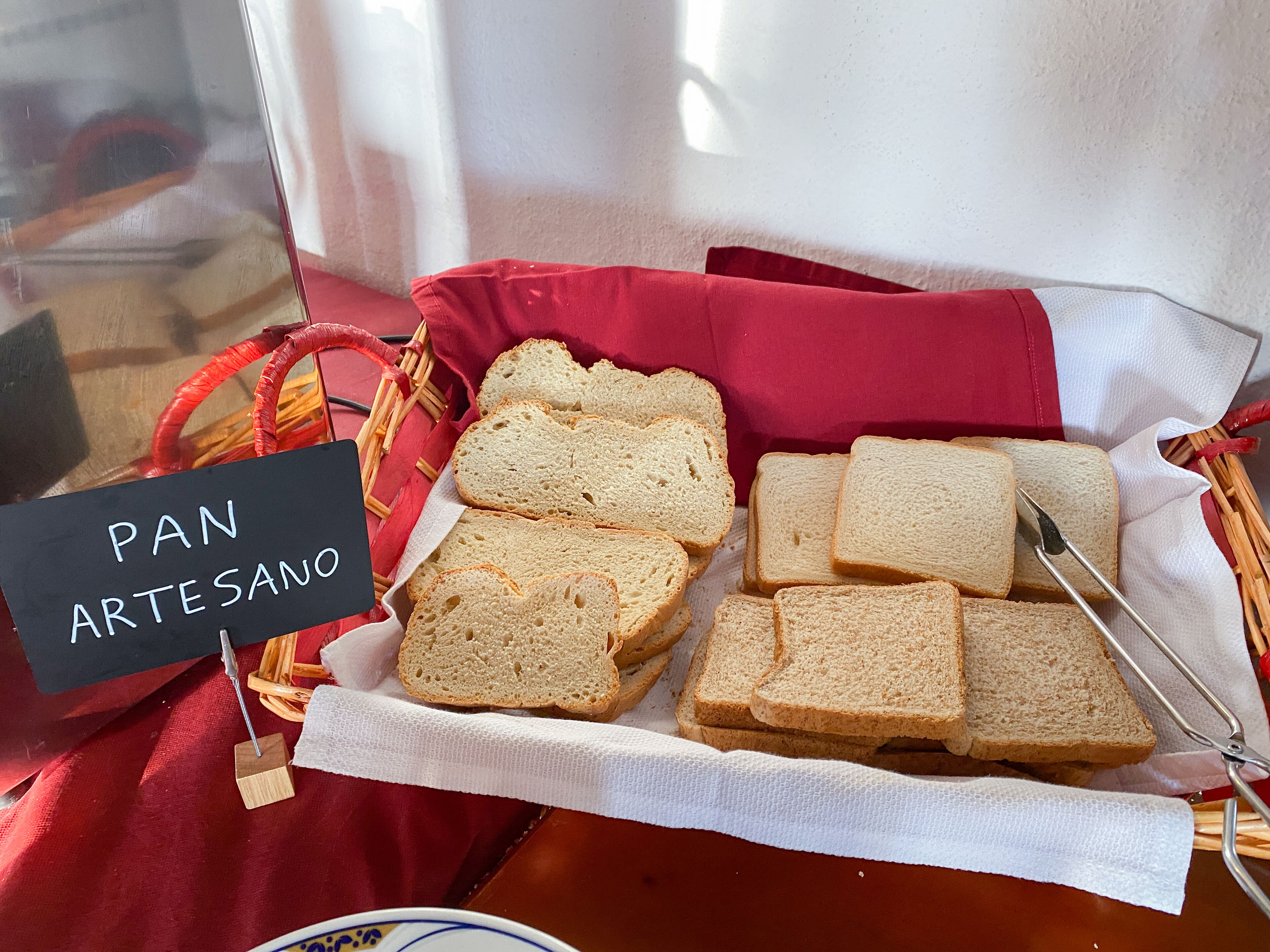 A basket of artisanal bread on a table with a sign reading "PAN ARTESANO".