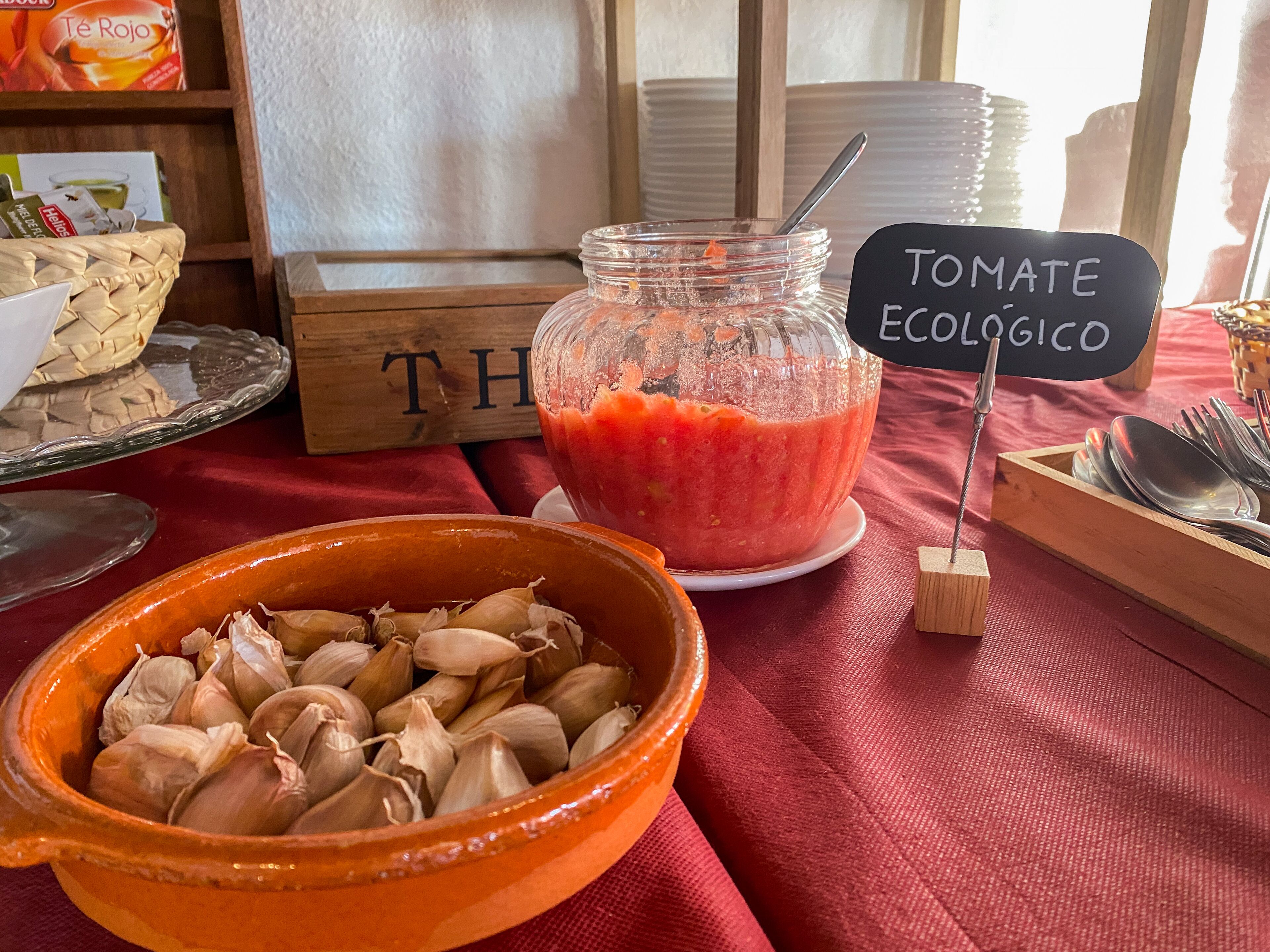 Una mesa con un cuenco de ajo, un frasco de salsa de tomate y un cartel que dice 'TOMATE ECOLOGICO'.