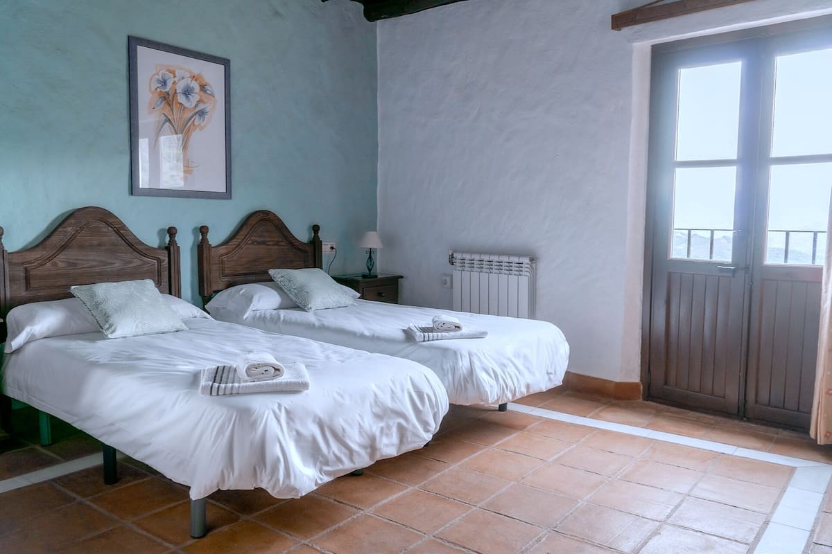 A room with two beds, a radiator, a door leading to a balcony, and a framed picture on the wall.