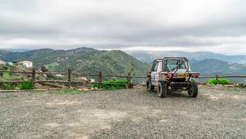 A rugged off-road vehicle parked on a gravel path with a wooden fence and a mountainous backdrop.