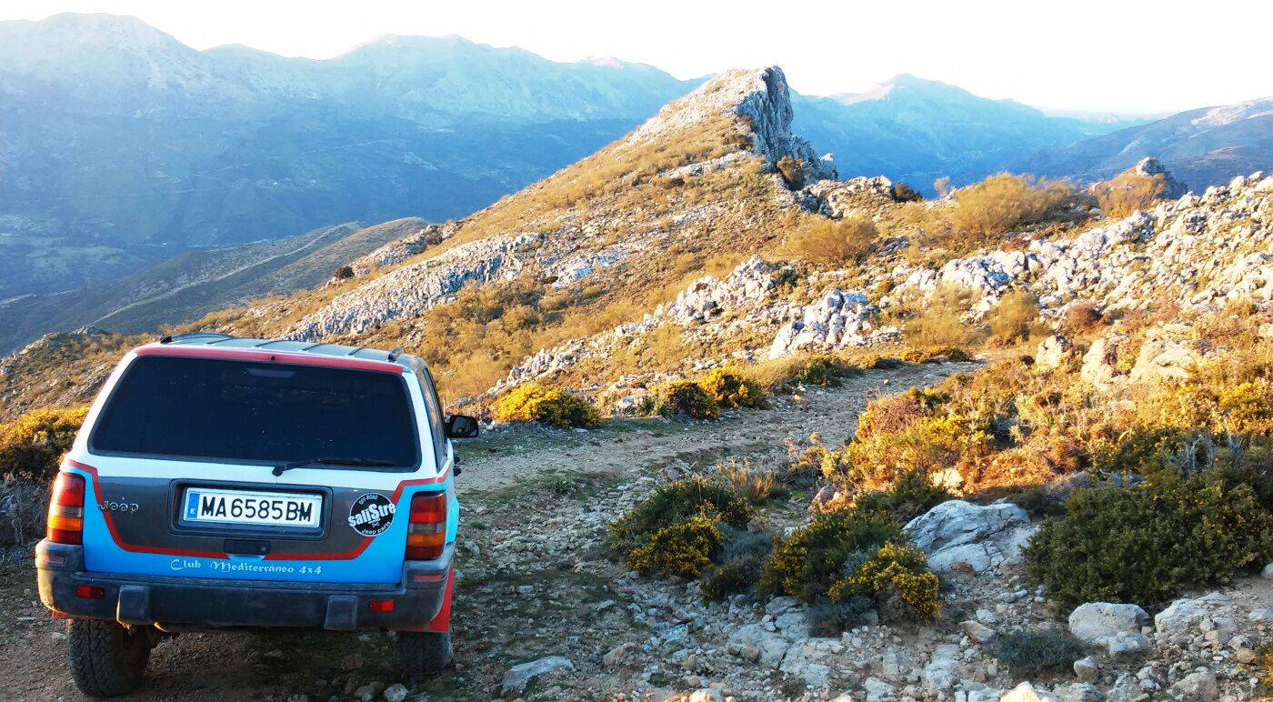 A Jeep Club Mediterraneo 4x4 vehicle parked on a rocky mountain path with a mountainous landscape in the background.