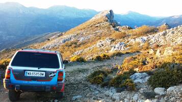 A Jeep Club Mediterraneo 4x4 vehicle parked on a rocky mountain path with a mountainous landscape in the background.