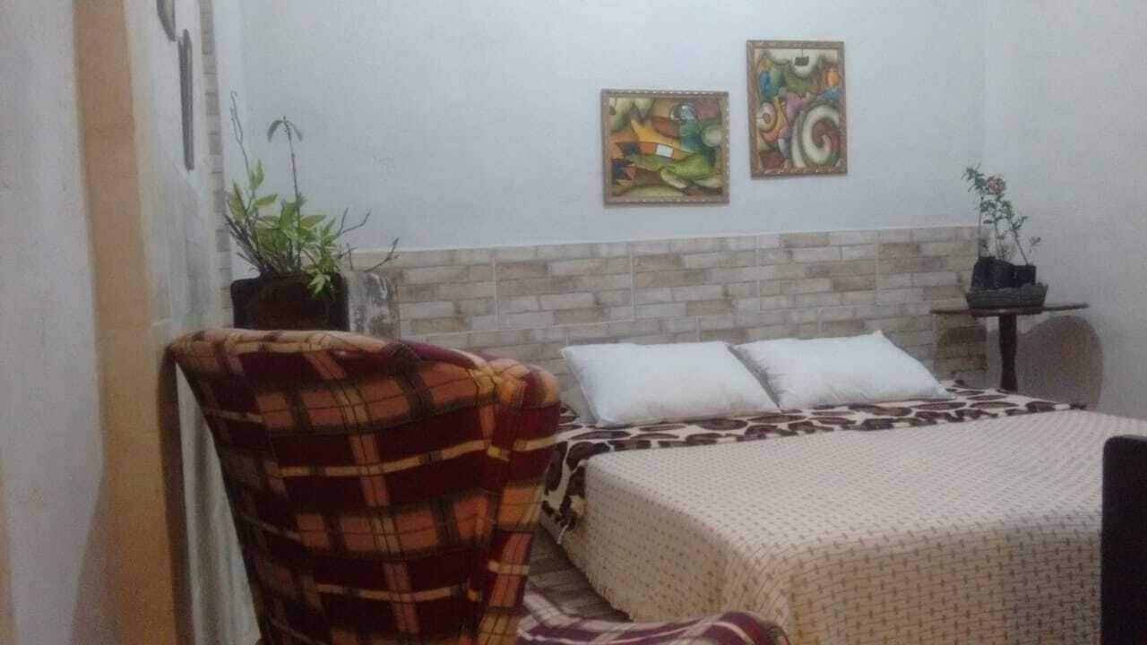 Un dormitorio con una cama, una silla, dos cuadros y una planta en maceta.