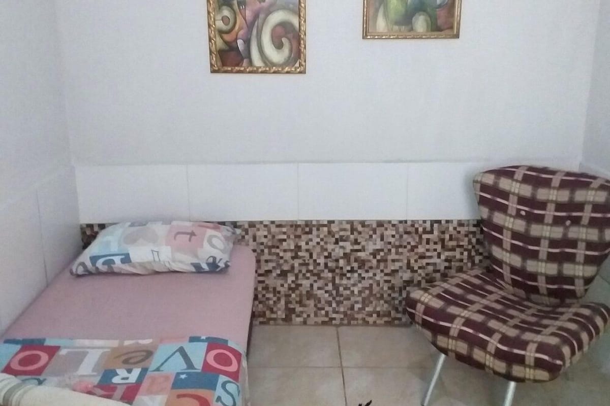 A room with a bed, a chair, and two abstract paintings on the wall.