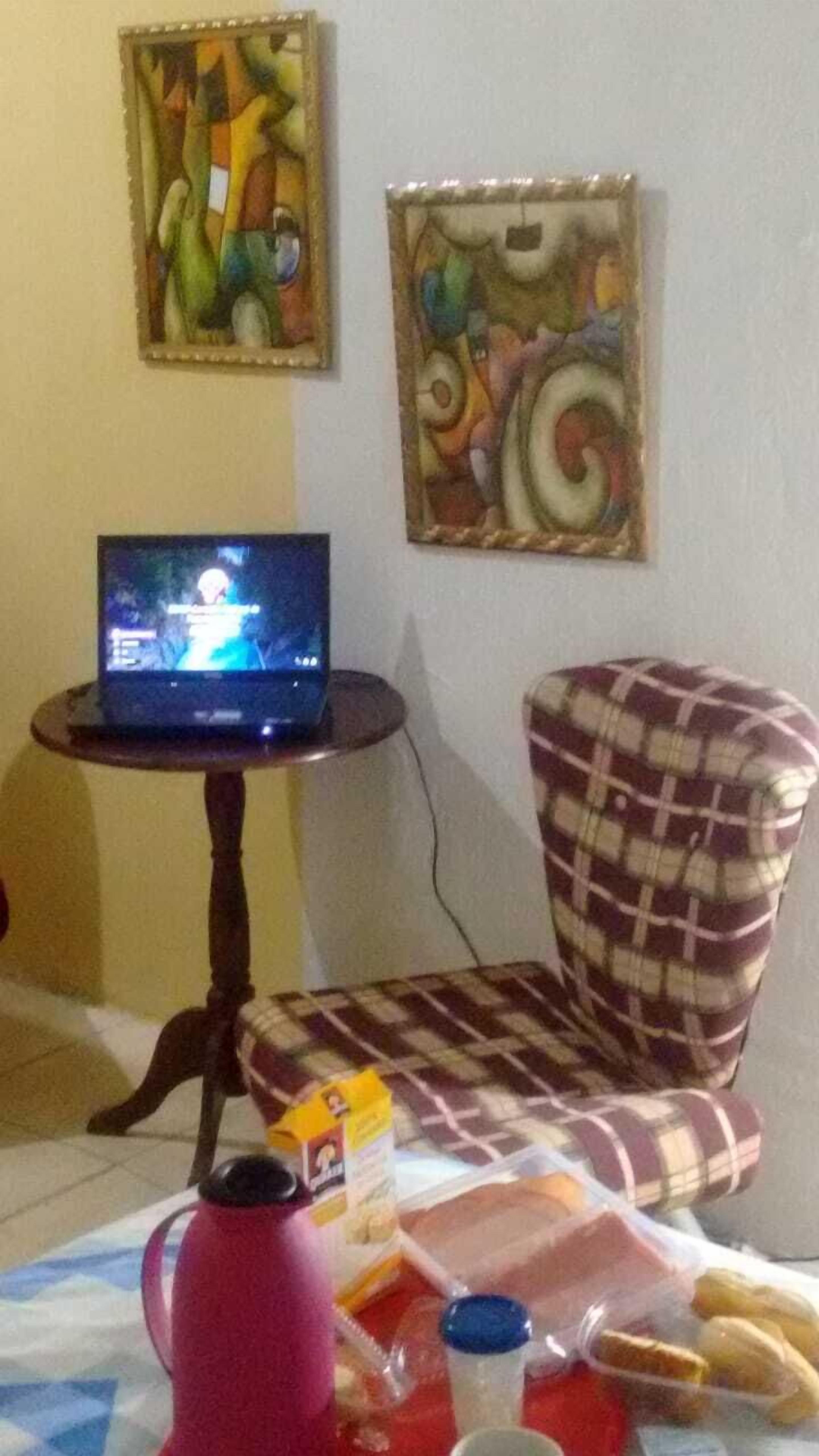 Habitació amb un ordinador portàtil sobre una taula petita, una cadira escocesa, una paperera vermella i un recipient de plàstic amb aliments.