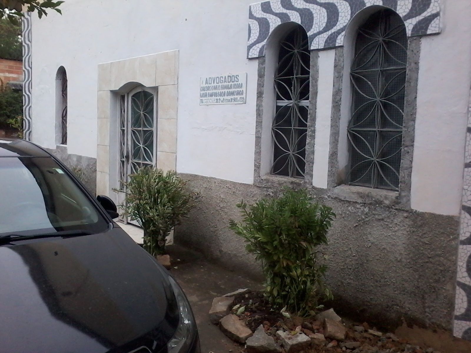 Un edificio con un letrero que dice "AVOGADOS" y tres ventanas arqueadas con celosías metálicas decorativas.