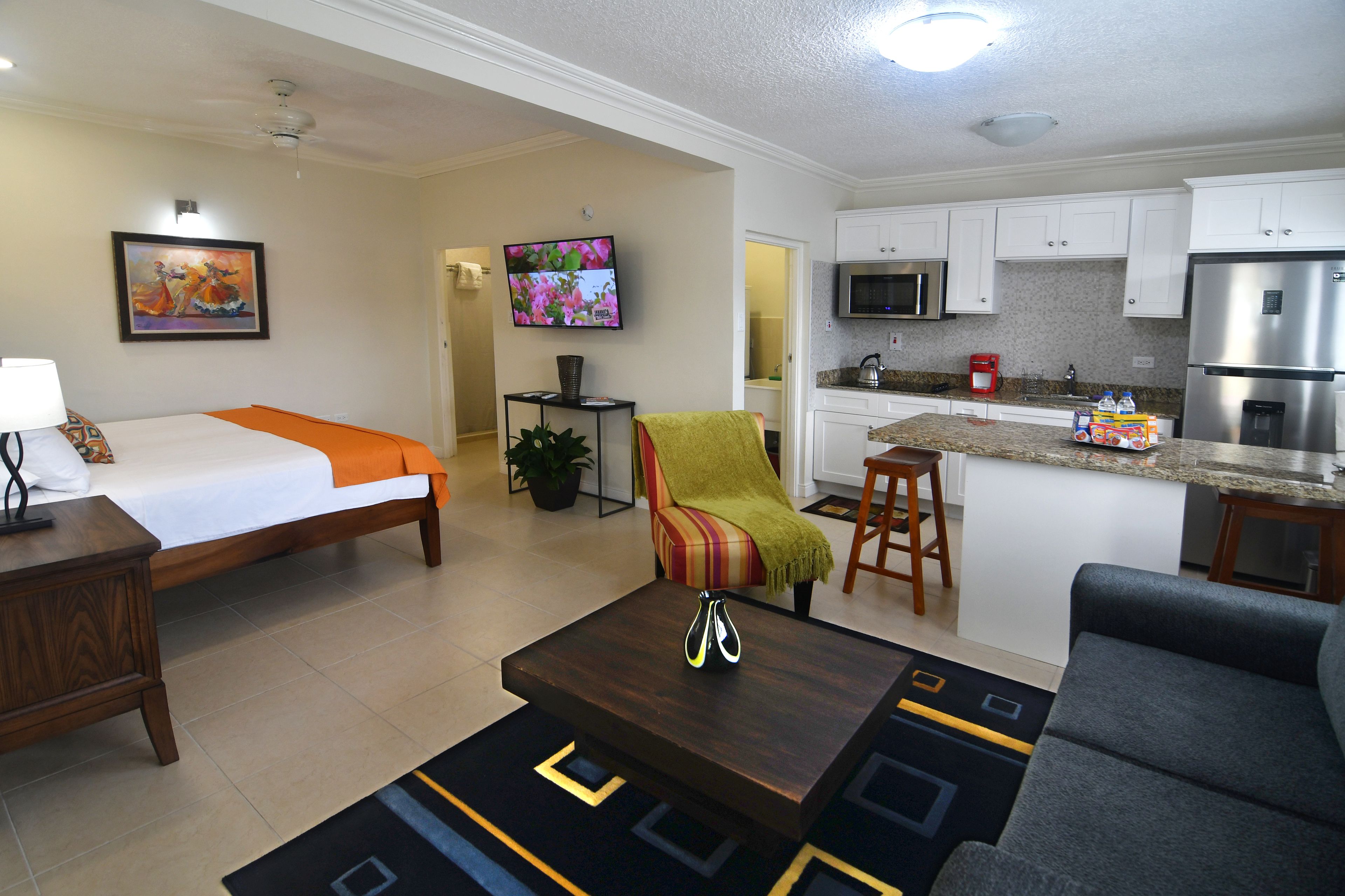Una habitación de hotel moderna con cama, sofá, mesa de centro, televisor, zona de cocina y baño.