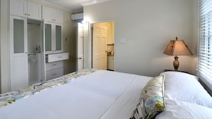 Une chambre à coucher avec un grand lit, une table de chevet avec une lampe, une armoire et une salle de bain visible à travers une porte ouverte.