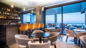 A bar area with a view of the sea, featuring round tables and chairs, and a well-stocked bar counter. - Radisson Blu Hotel, Larnaca (Larnaca)
