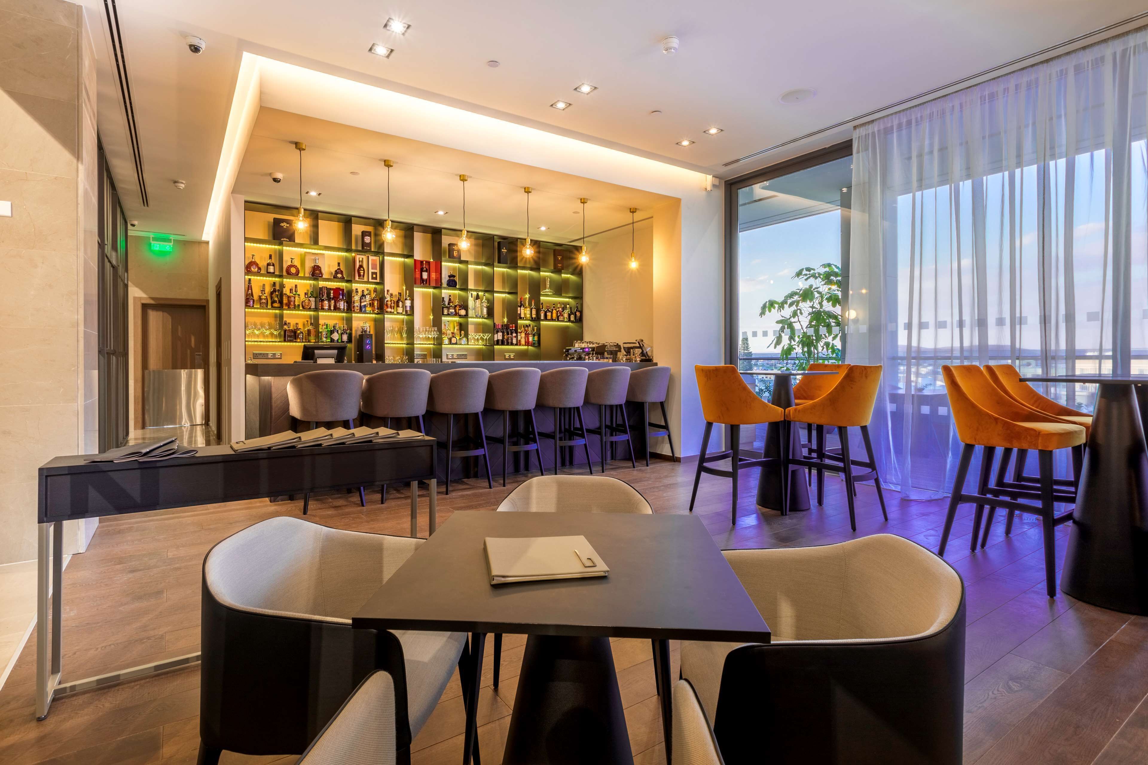 A modern bar area with a long counter, multiple bar stools, and a seating area with tables and chairs.