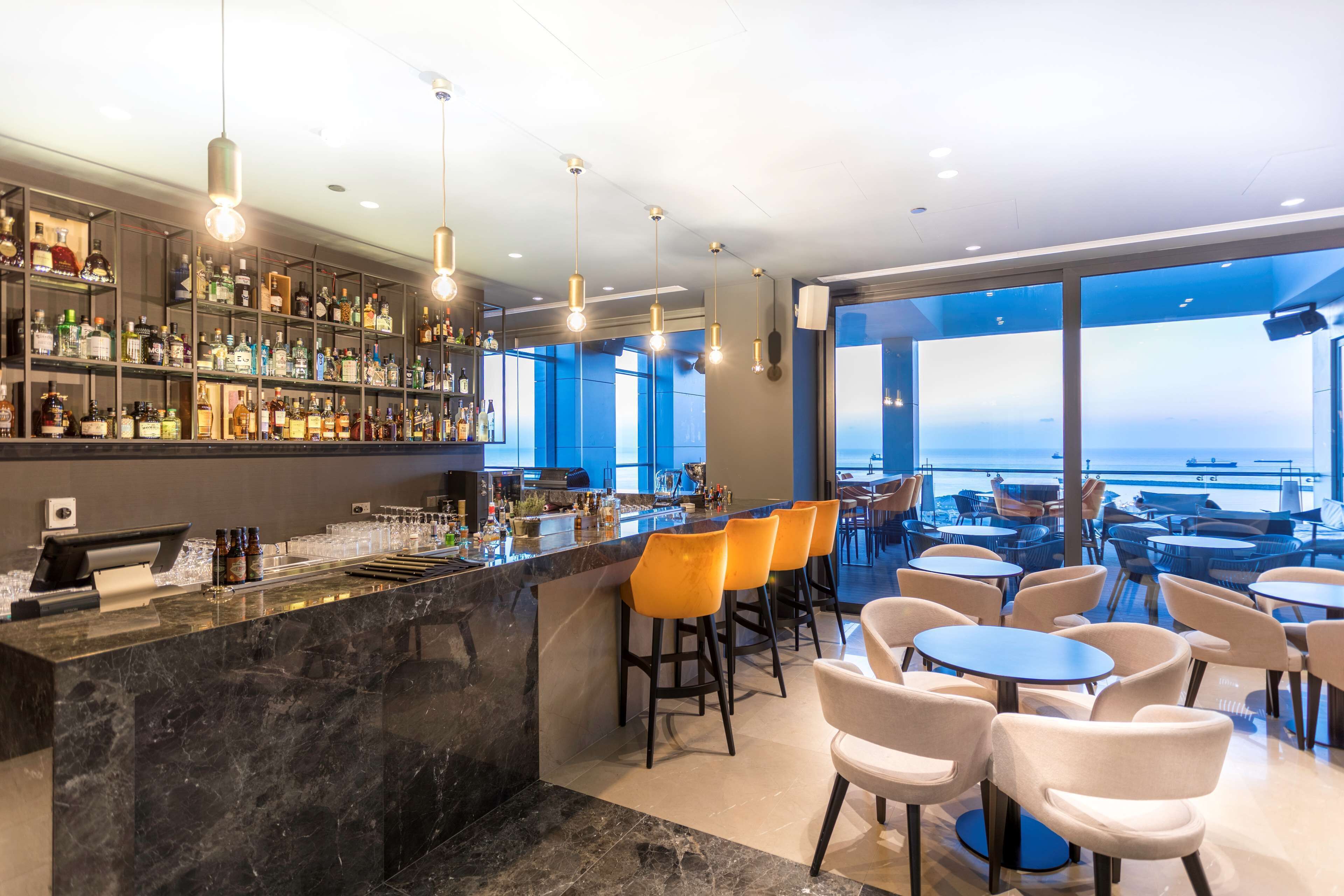 Een moderne bar met een marmeren aanrecht, diverse drankflessen en een zithoek met stoelen en tafels.