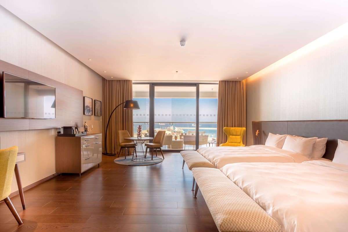 A modern hotel room with a large bed, a desk, a chair, and a view of the ocean.