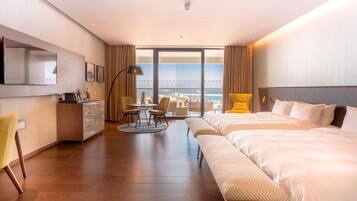 A modern hotel room with a large bed, a desk, a chair, and a view of the ocean.