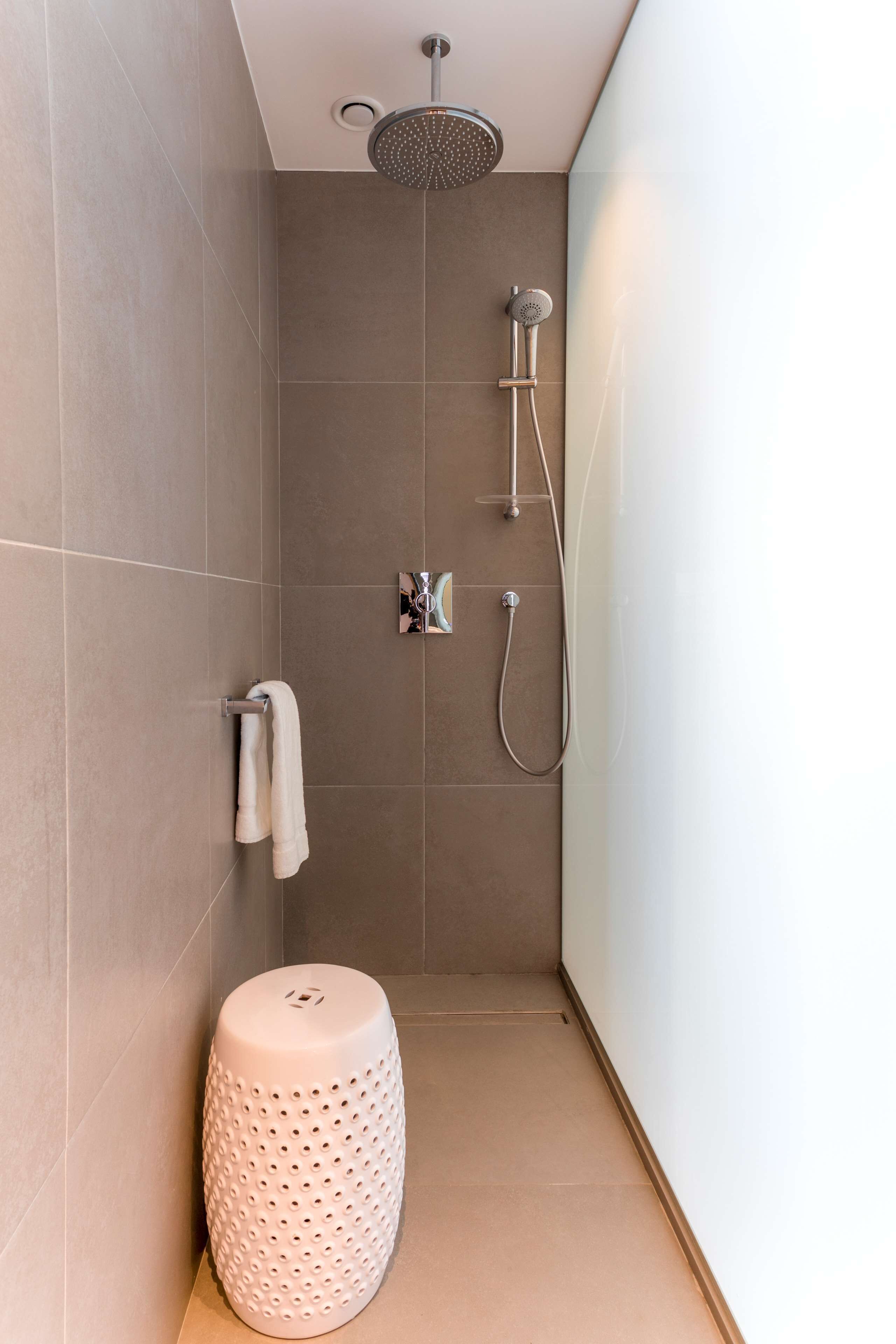 Un área de ducha moderna con un cabezal de ducha de mano, un grifo empotrado en la pared y un perchero con una toalla blanca.