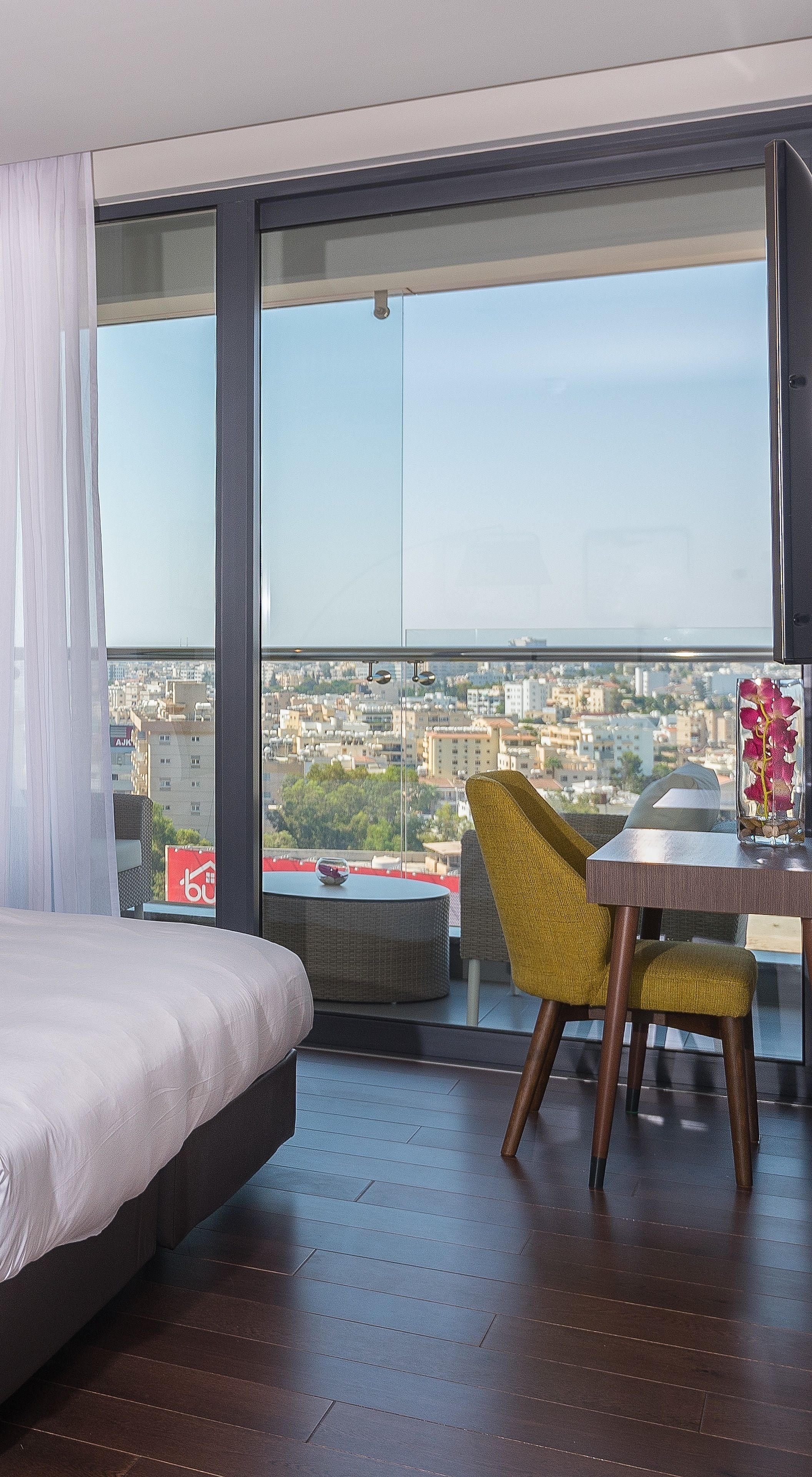 Ein modernes Hotelzimmer mit großem Fenster, einem Bett, einem Esstisch und einem gelben Sessel.